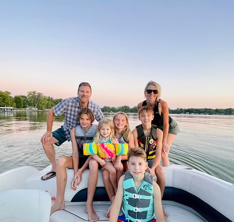 A family of seven posing together on a boat during sunset.